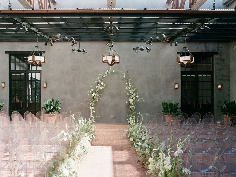 Ceremony on hotel patio with greenery arch and ghost chairs