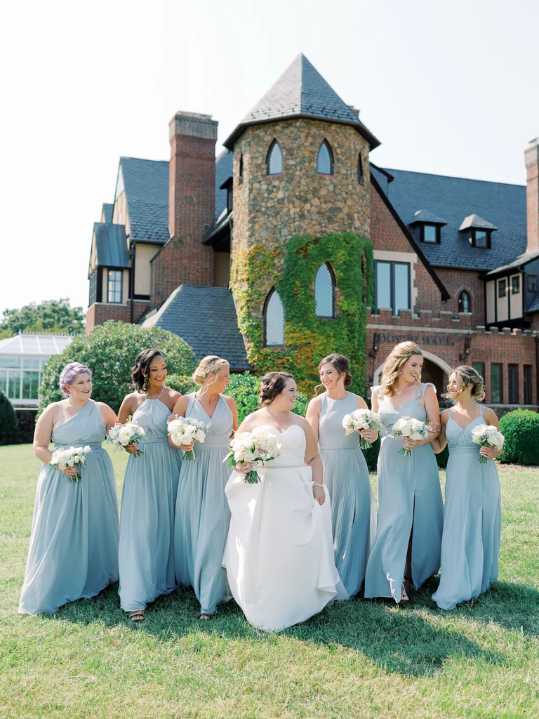 A bride walks with her wedding party over the lawn of their wedding venue.