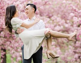 Man lifting up woman in engagement photo with cherry trees in the background