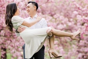 Man lifting up woman in engagement photo with cherry trees in the background