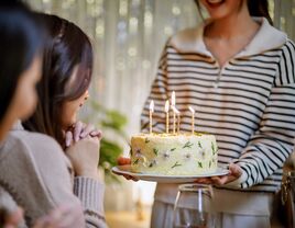 Woman bringing birthday cake with lighted candles to sister-in-law