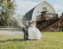 Couple celebrating with a popped bottle of champagne outside the barn venue