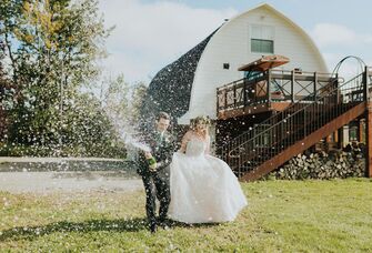 Couple celebrating with a popped bottle of champagne outside the barn venue