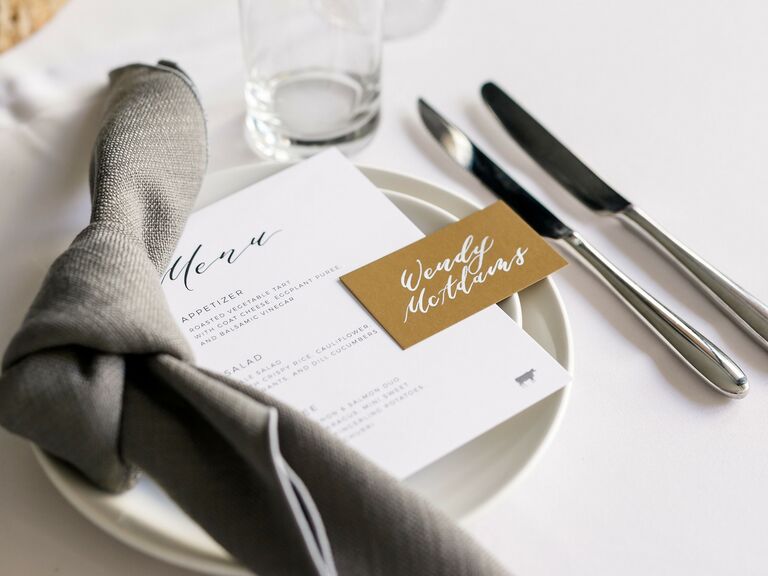 modern wedding reception place setting with gray tied napkin and gold place card with white calligraphy