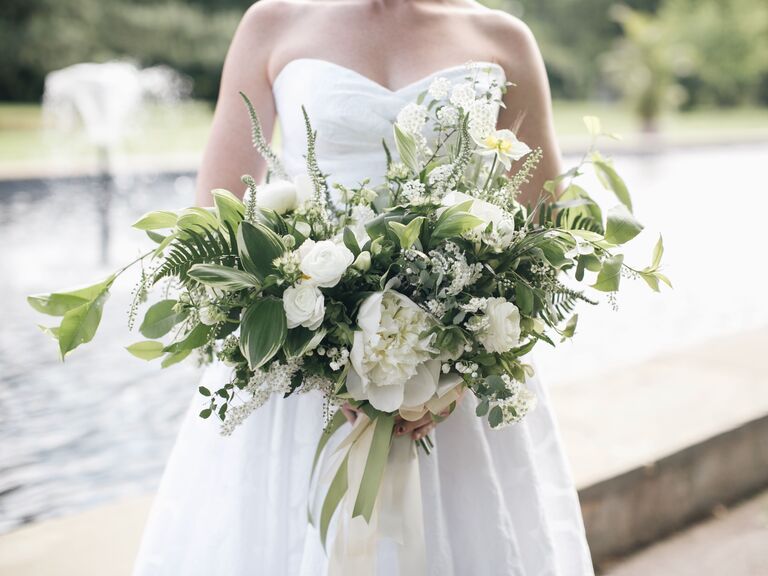 A bride holds an overflowing bouquet of greenery and white flowers.