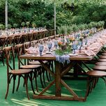 long wooden table with wooden cross back chairs and blue water goblets lining the table