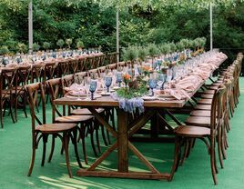 long wooden table with wooden cross back chairs and blue water goblets lining the table