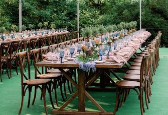 long wooden table with wooden cross back chairs and blue water goblets lining the table