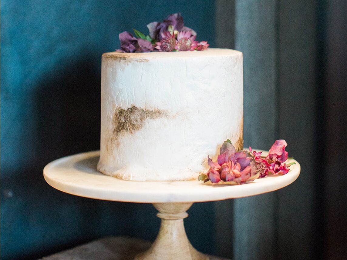 A white engagement cake decorated with pink and purple flowers