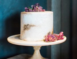 A white engagement cake decorated with pink and purple flowers