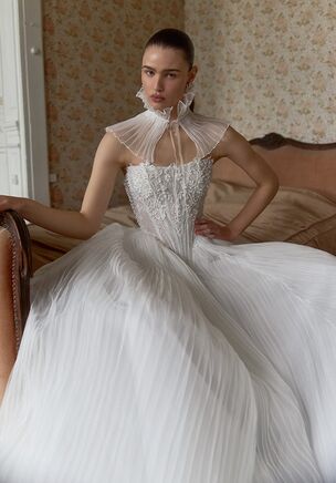 A strapless sweetheart neckline frames bare shoulders in an Ivory lace and textured fabric gown. Textured embroidery and delicate beading bloom across a translucent overlay. Below, a sculpted basque waistline yields to a sweeping skirt. A low, open back balances a chapel-length train. A coordinating choker transforms it into a high-neck arrangement, defining the Eclair gown from WONÃ Concept's White collection.