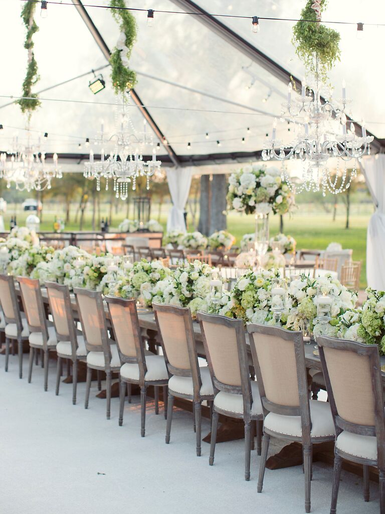 luxury wedding reception with long banquet table beneath glass chandeliers with low white centerpieces decorating the table