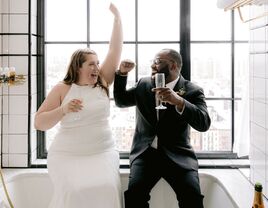 bride and groom toasting champagne in bathtub