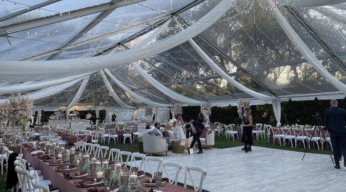 Elegant wedding reception under a clear tent with draped fabric and lights at The Roundtree Amagansett