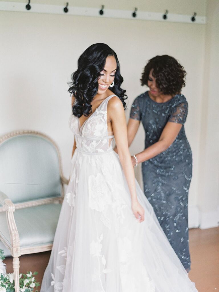 bride wearing tulle wedding dress gets ready with mom who is buttoning the back of bride's dress