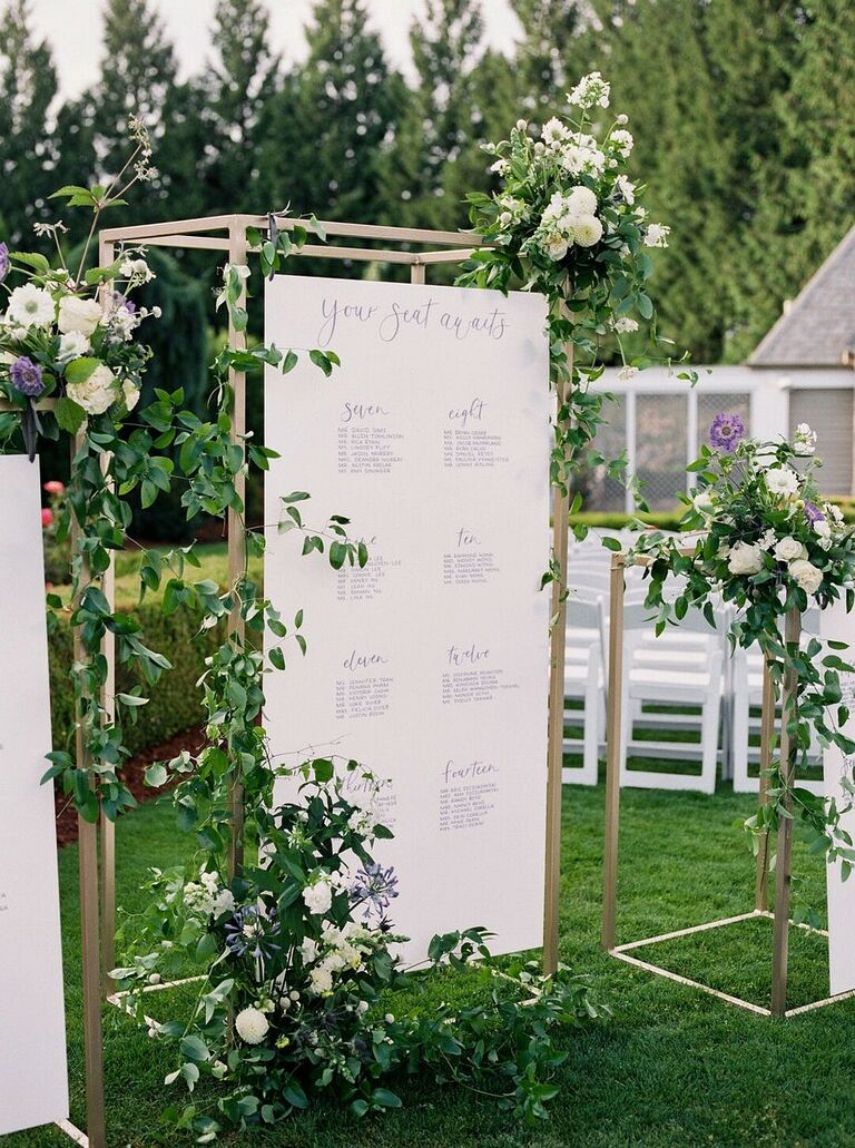Seating chart suspended from gold structure and covered in greenery