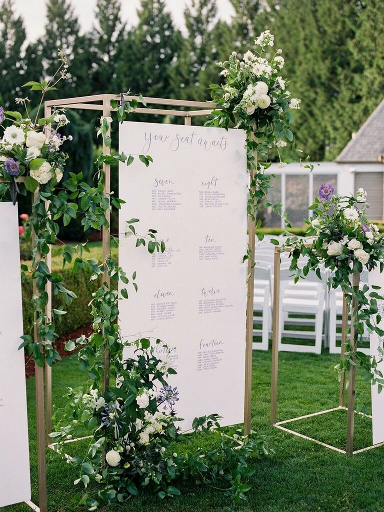 Seating chart suspended from gold structure and covered in greenery