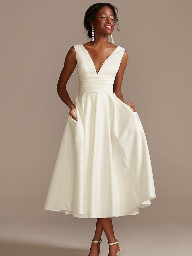 Model wears a white tea-length dress with a full skirt and a plunging neckline. 