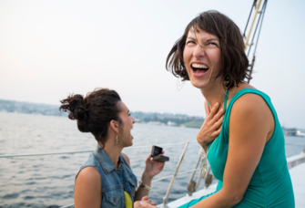 Woman proposing to partner on boat while smiling and laughing