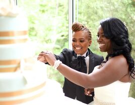 Couple cutting their wedding cake in front of guests during wedding reception.