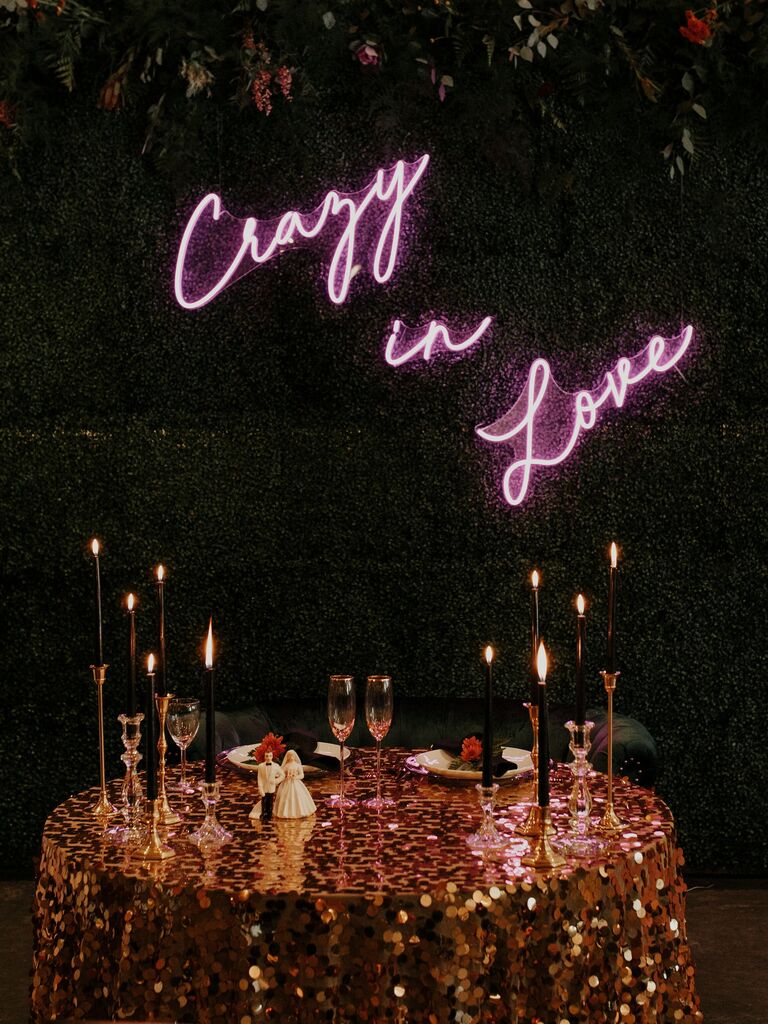 modern sweetheart table decor with gold sequined tablecloth and pink neon sign backdrop that says crazy in love