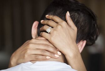 couple embracing with woman's hands with engagement ring behind man's neck