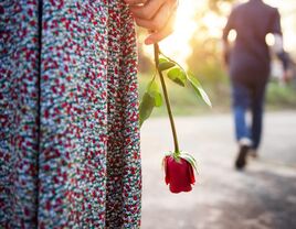 Woman holding a rose while a man walks away