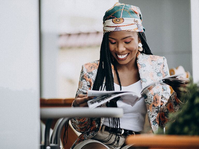 Woman in a floral blazer and matching headwrap reading a magazine.