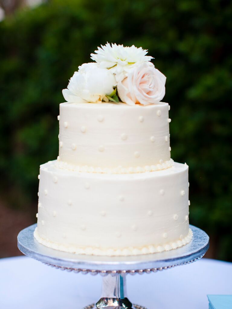 two tier wedding cake decorated with smooth buttercream icing, piped polka dots and ivory flowers on top