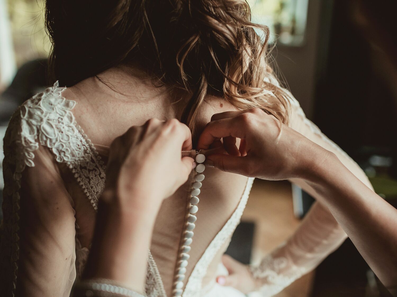woman getting buttoned into wedding dress