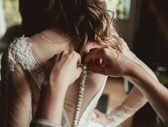 woman getting buttoned into wedding dress
