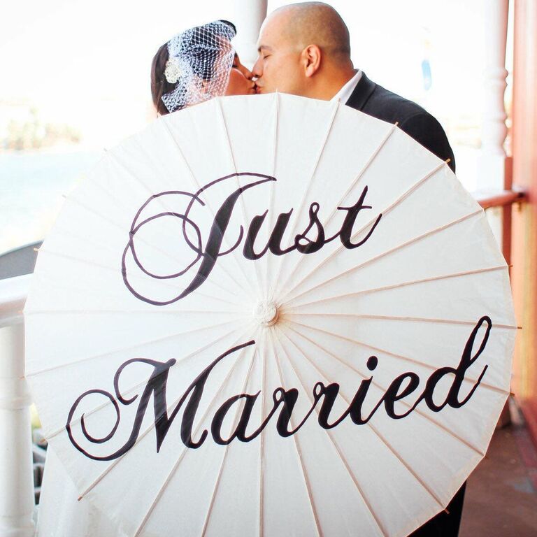 Couple shares a sweet kiss while showing off their custom wedding parasol that reads 