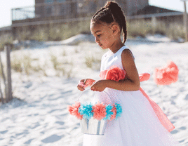 Flower girl walking on sandy beach.