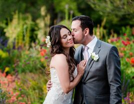Newlyweds share a sweet kiss surrorunded by colorful flowers in a lush garden. 