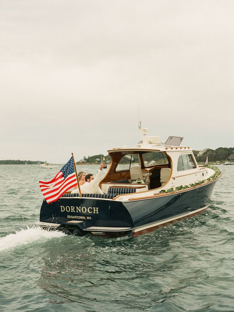 bride and groom leaving wedding reception on sailboat with american flag waving on the back
