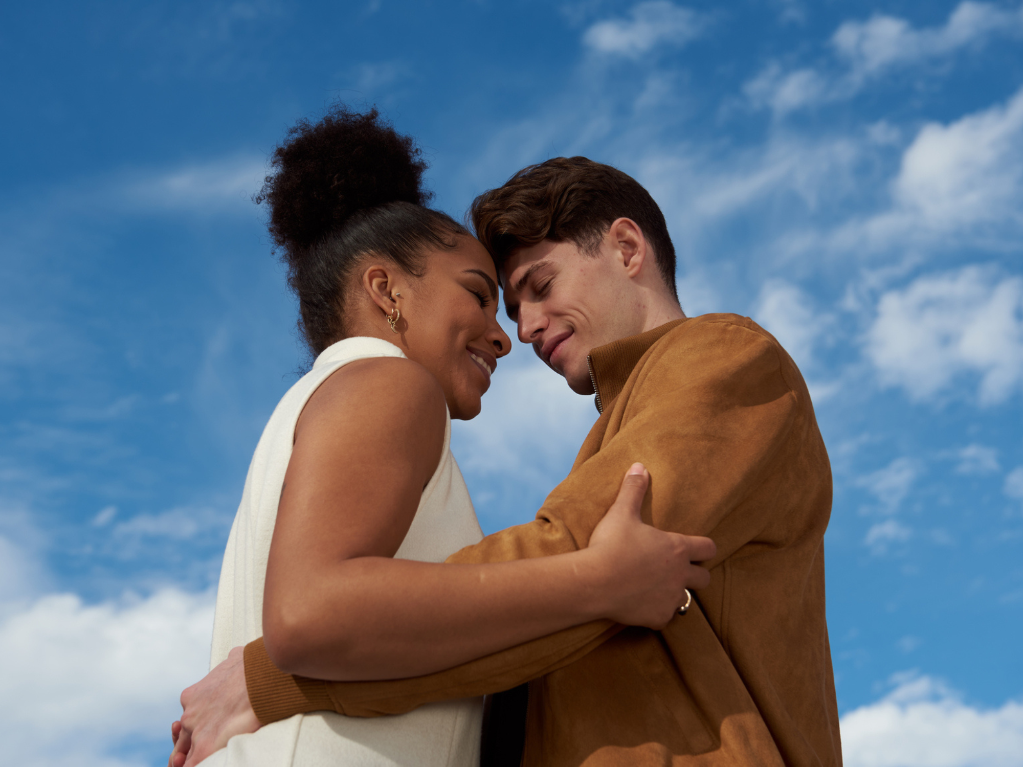 Couple hugging in front of blue sky, questions to build trust in a relationship