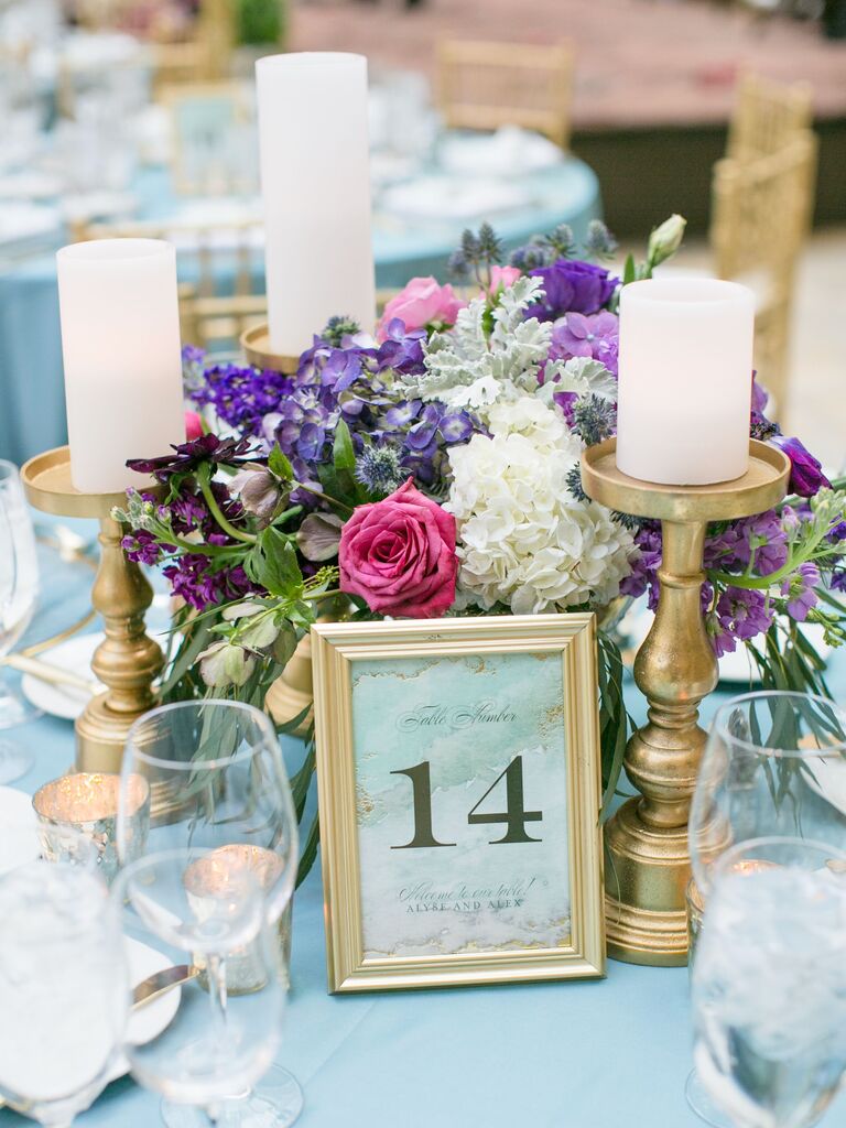 small pink, purple and white wedding centerpiece with white pillar candles on gold candlesticks