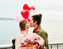 Couple kissing on boardwalk holding heart shaped balloons