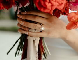 Hand wearing engagement ring and holding bouquet