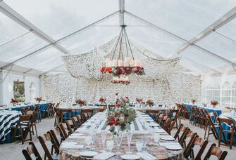 Wedding reception inside a clear enclosed event tent with a hanging chandleier and decor