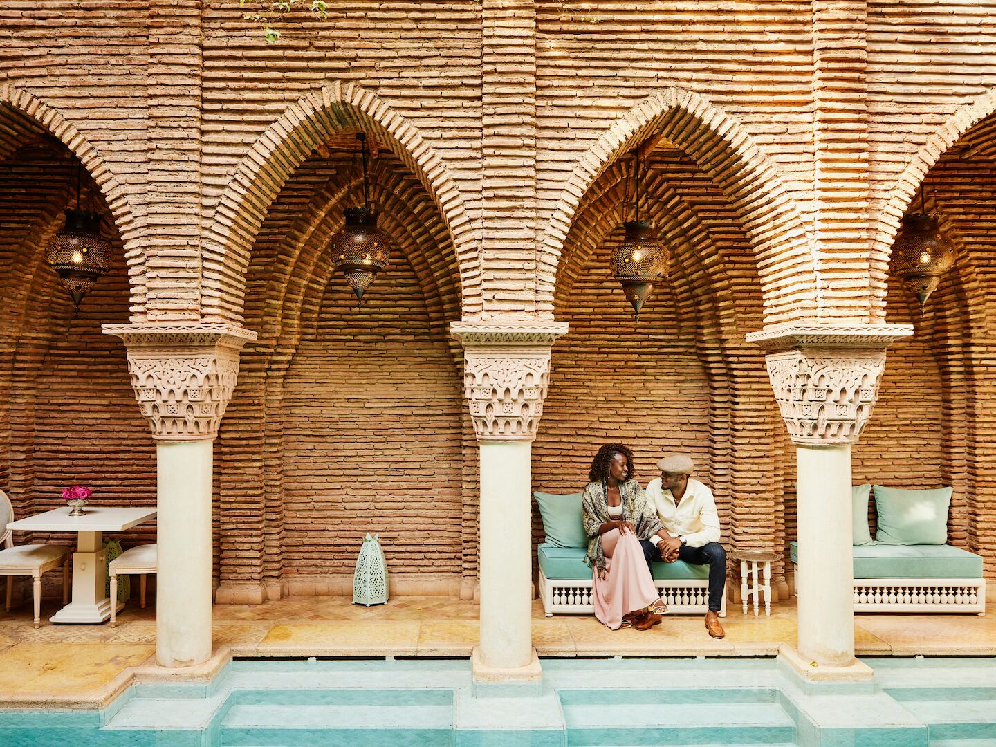 Wide shot of couple holding hands while sitting in courtyard of luxury hotel
