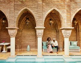 Wide shot of couple holding hands while sitting in courtyard of luxury hotel