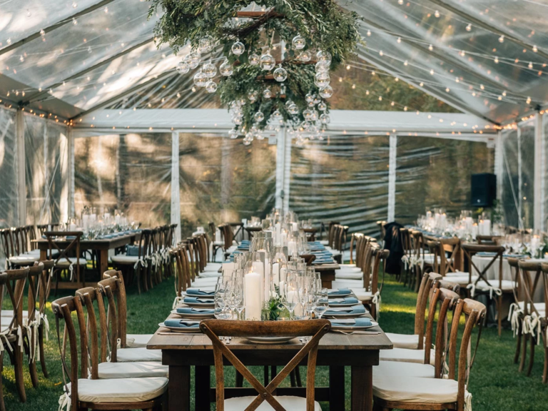 Clear tent reception space with wooden tables and chairs with hanging foliage