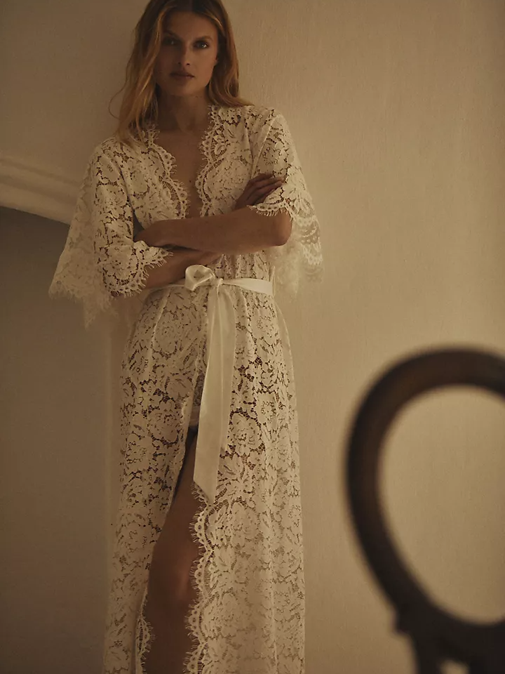 Model wearing a white lace bridal robe with a matching bow around the waist