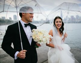 Bride and groom holding umbrellas on rainy wedding day