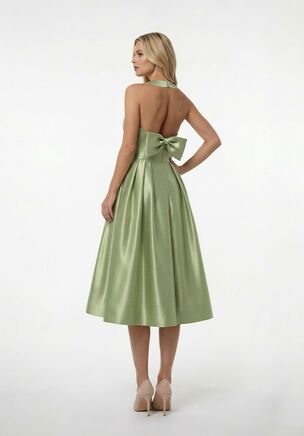 A modern bridesmaid dress designed for unforgettable entrances and effortless movement, this midi-length style is crafted in Mikado with a flattering halter neckline that flows into a sleek V-neck. The full A-line skirt features soft pleats for beautiful structure and fluid movement, while the open back adds a fresh, unexpected touch, finished with a statement bow that ties the look together. Perfect for weddings that call for something elevated yet fun, this dress transitions seamlessly from ceremony to celebration. Available in floor length as style B283073A.