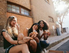 Group of freinds sitting on sidewalk eating pizza