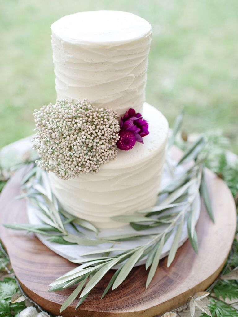 two tier textured buttercream wedding cake with greenery branches and bright purple flowers