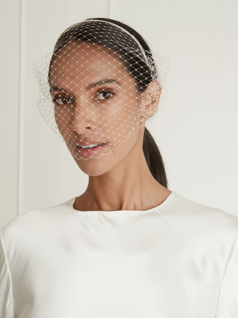 Model wears a headband with a birdcage veil attached. 