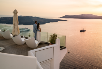 10-year anniversary trip ideas - couple standing on terrace at sunset in Greece